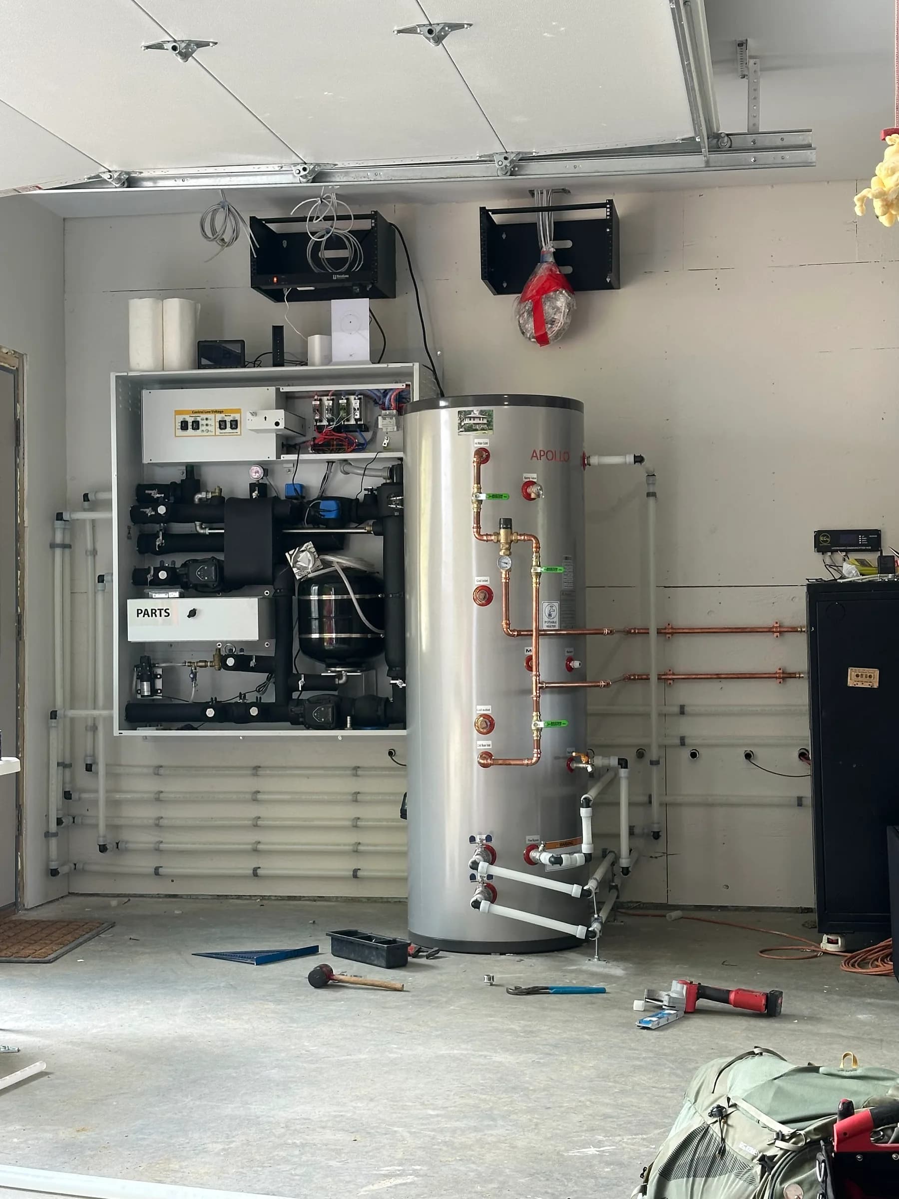 An air to water panel and a tall storage tank part way through installation with hand tools on the floor