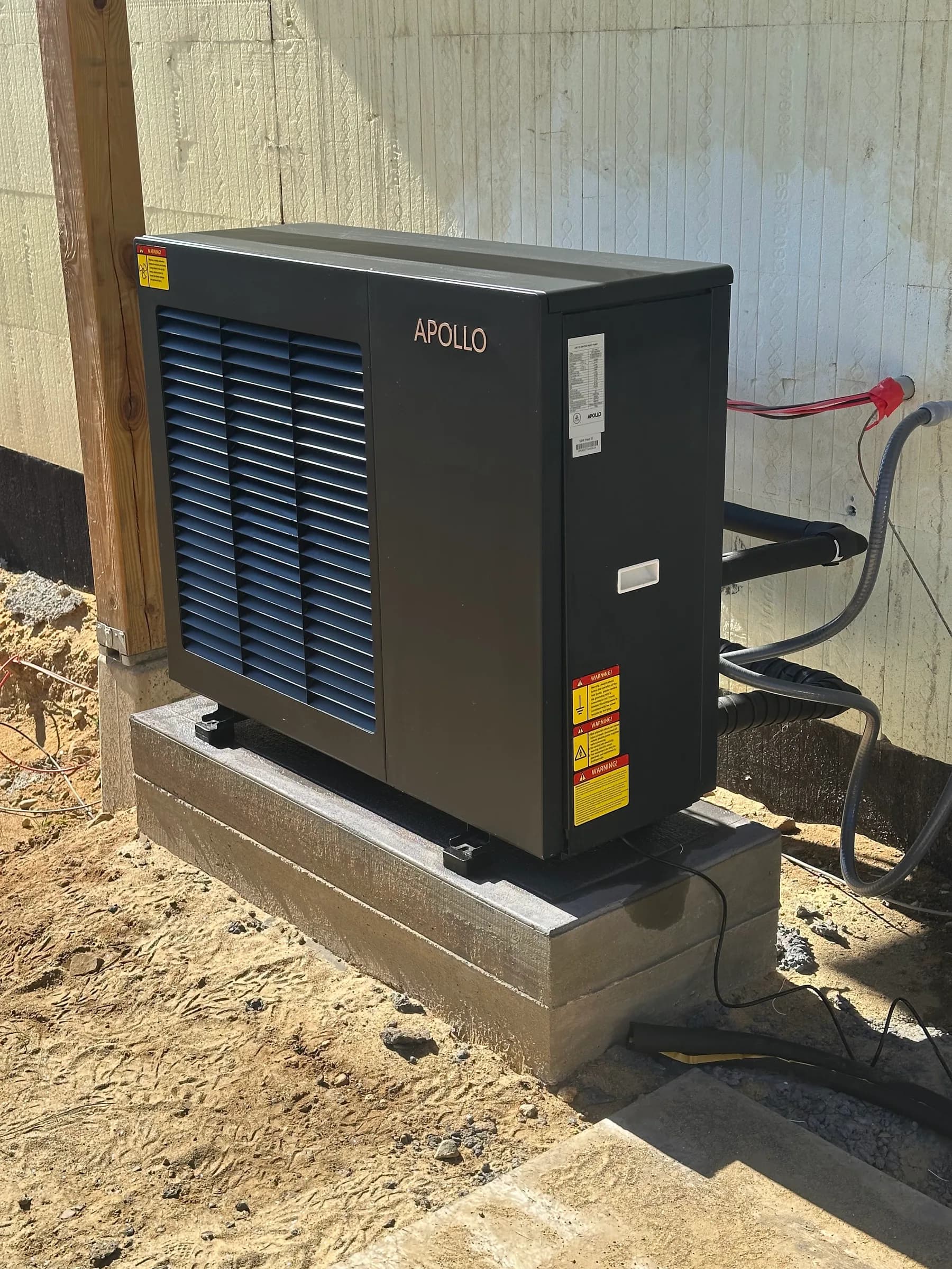An air to water heat pump outdoor unit on a raised concrete pad against a board and batten wall