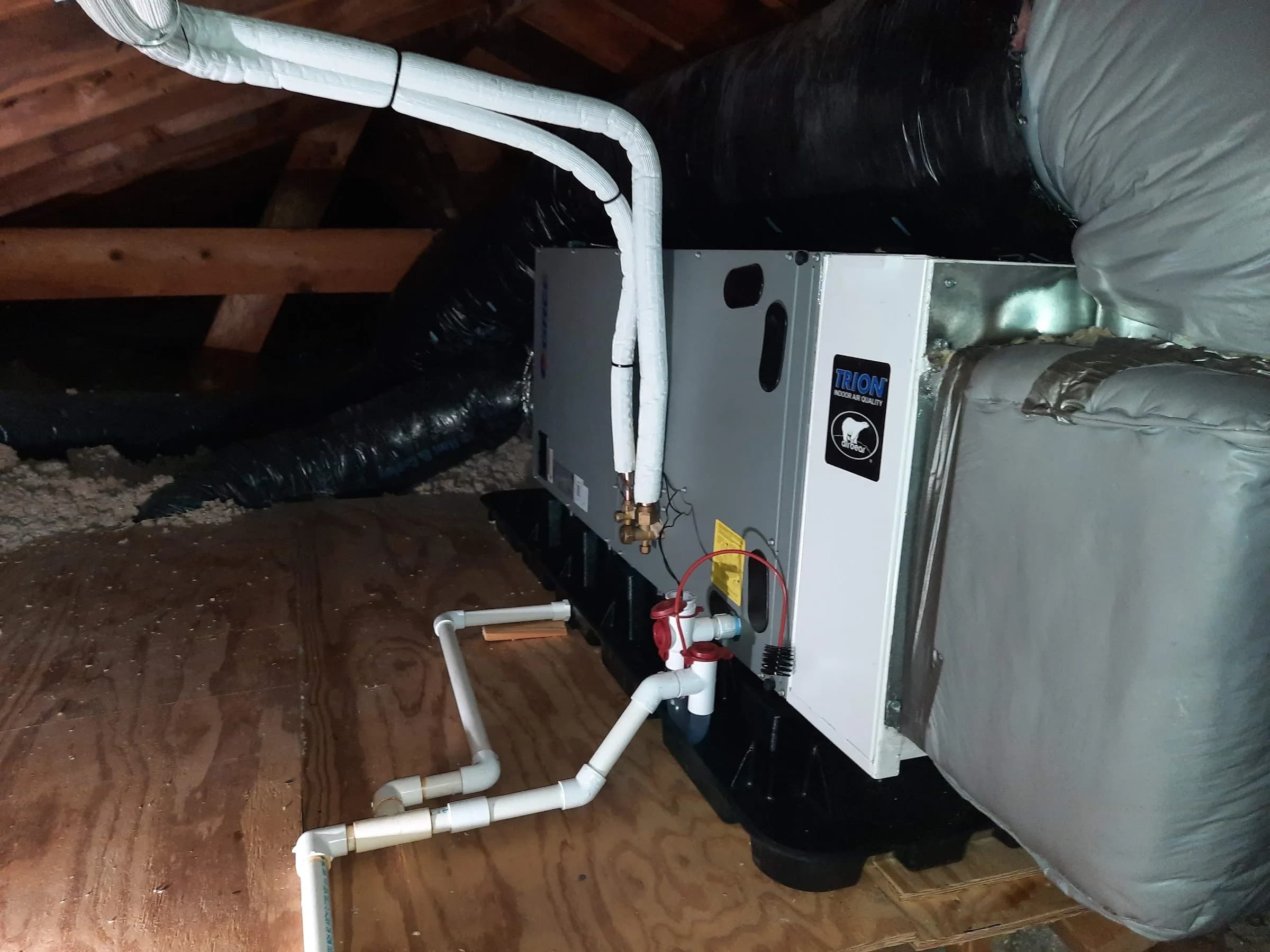 An air handler in an attic with insulated flexible duct and a condensate line running across the deck