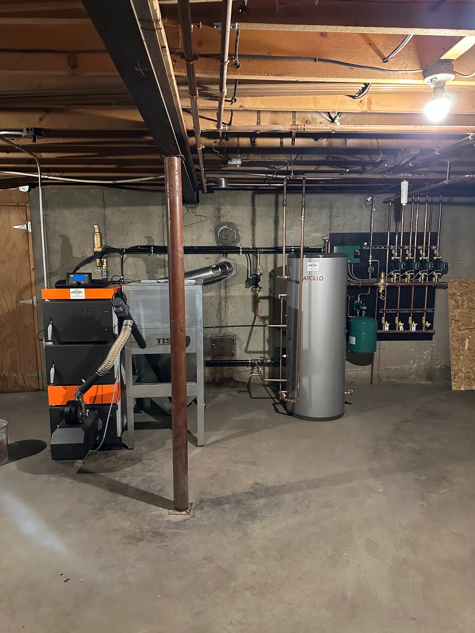 A basement mechanical room with a boiler, a storage tank and a zone manifold on copper piping