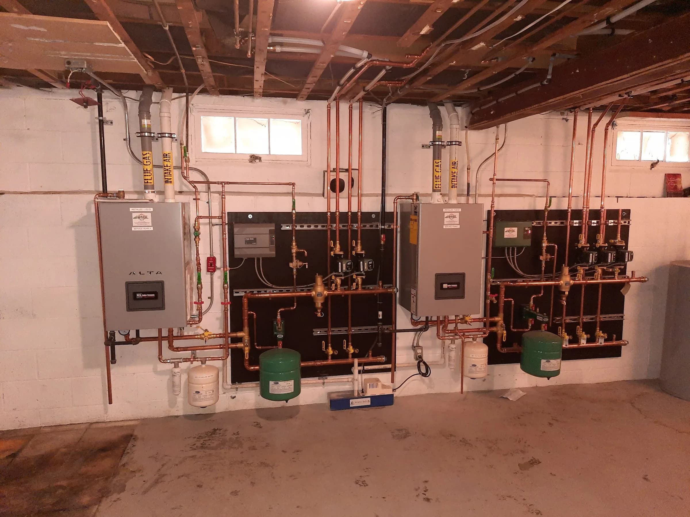 A basement wall carrying three control panels, copper piping and pumps for a multi zone heating system