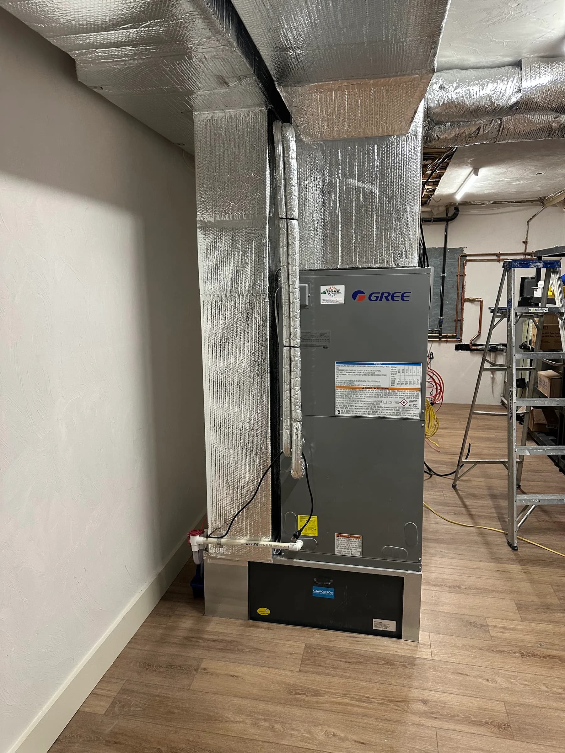 A ducted air handler and insulated supply plenum in a basement with a step ladder alongside