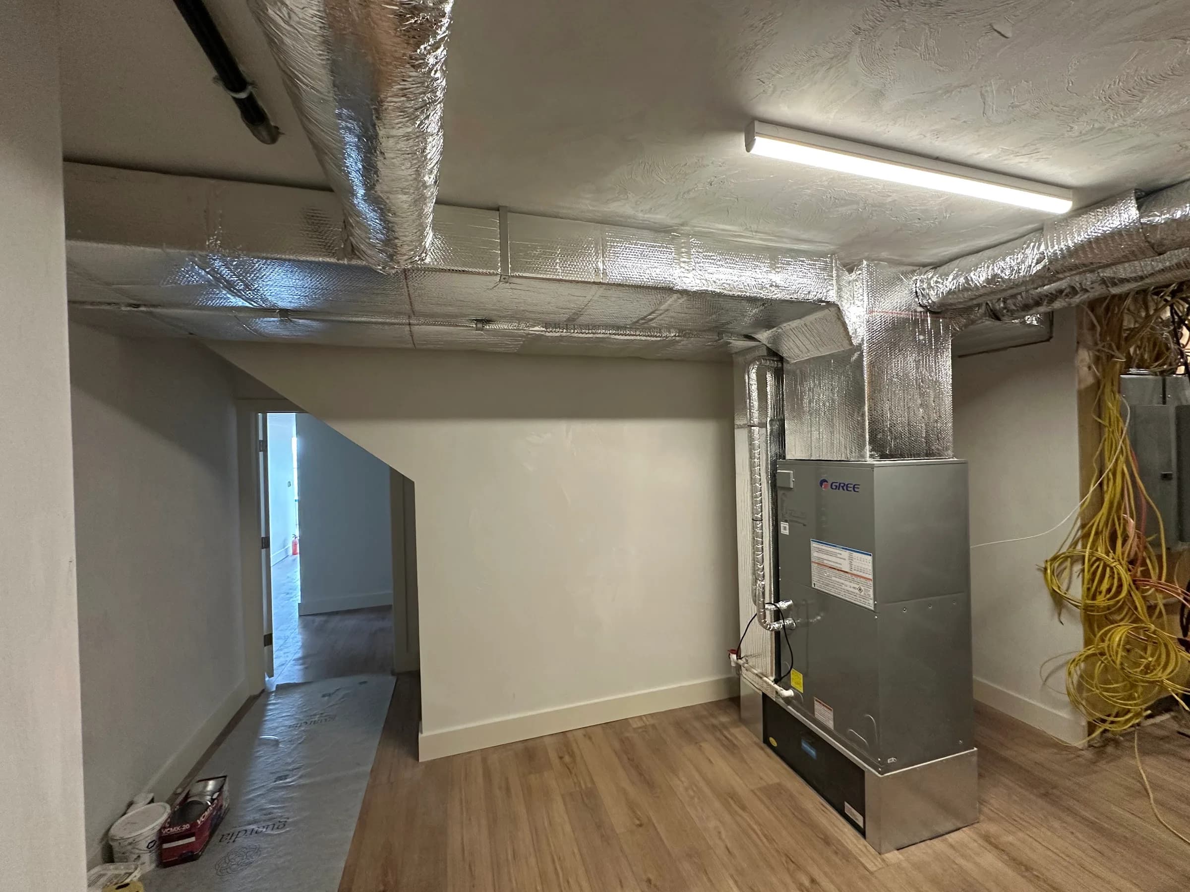 An indoor air handler and insulated trunk duct in a room with new wood flooring and unfinished walls