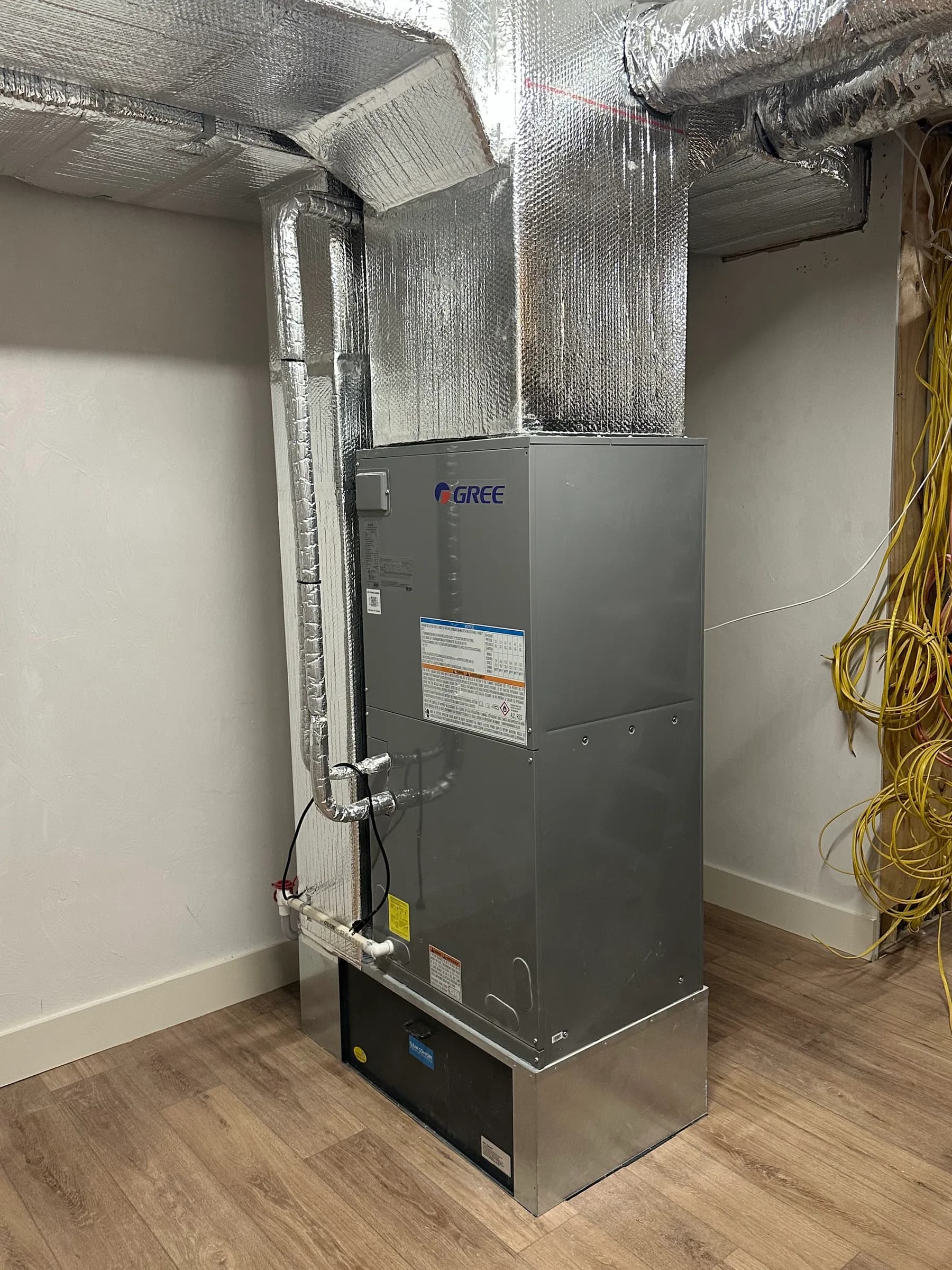 A vertical ducted air handler with insulated round ducts and a supply plenum in a finished room