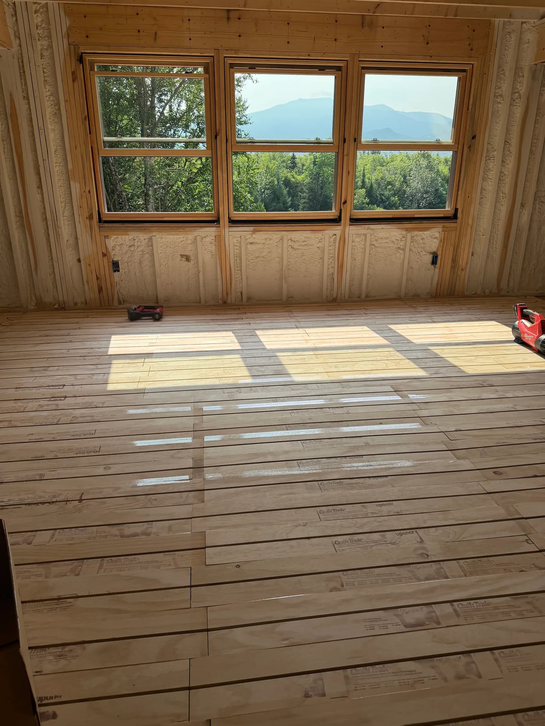 A pine framed room with a wide window looking toward a mountain and new wood flooring