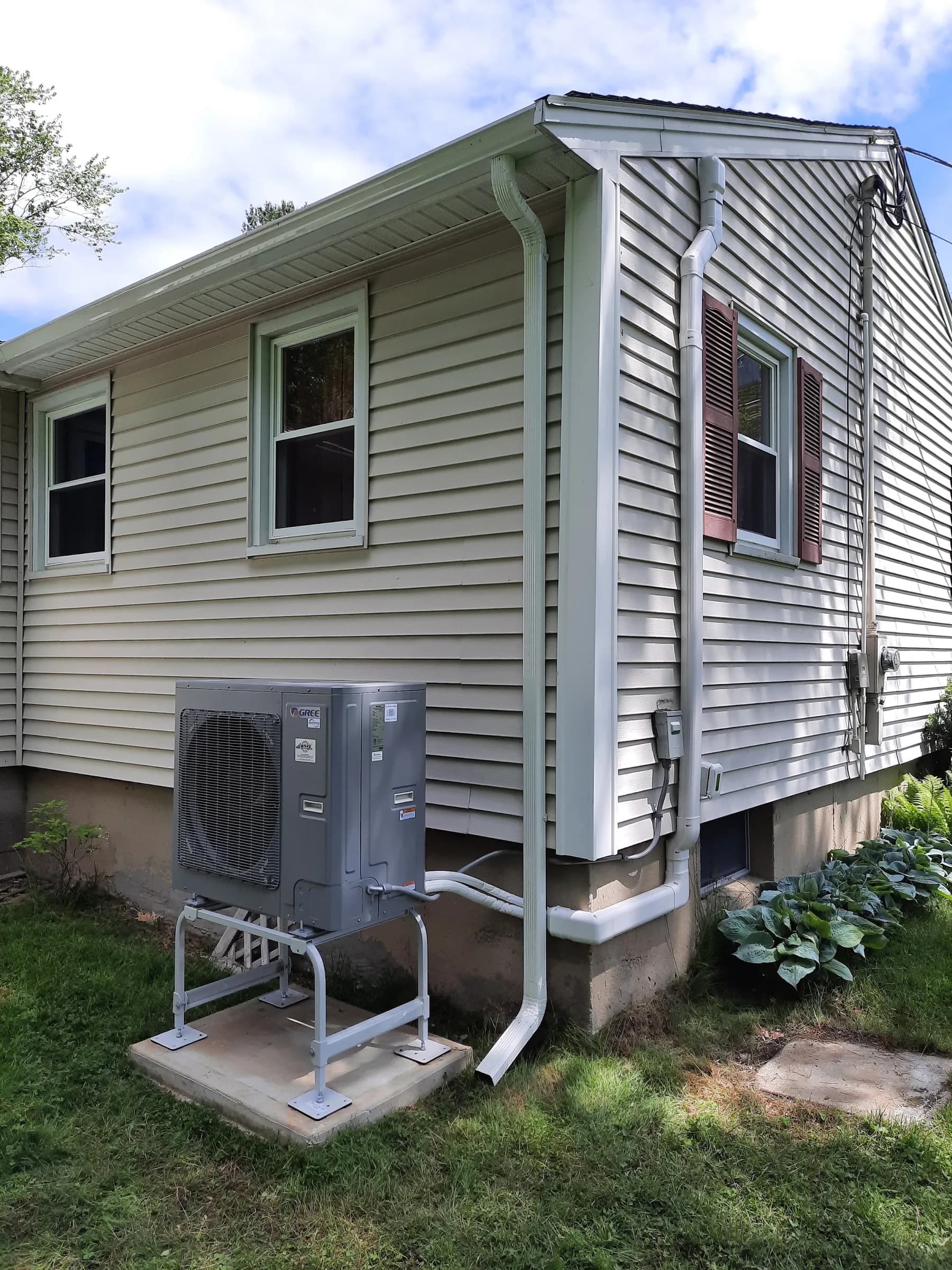An outdoor heat pump unit on a stand beside a downspout with the lineset run down the siding