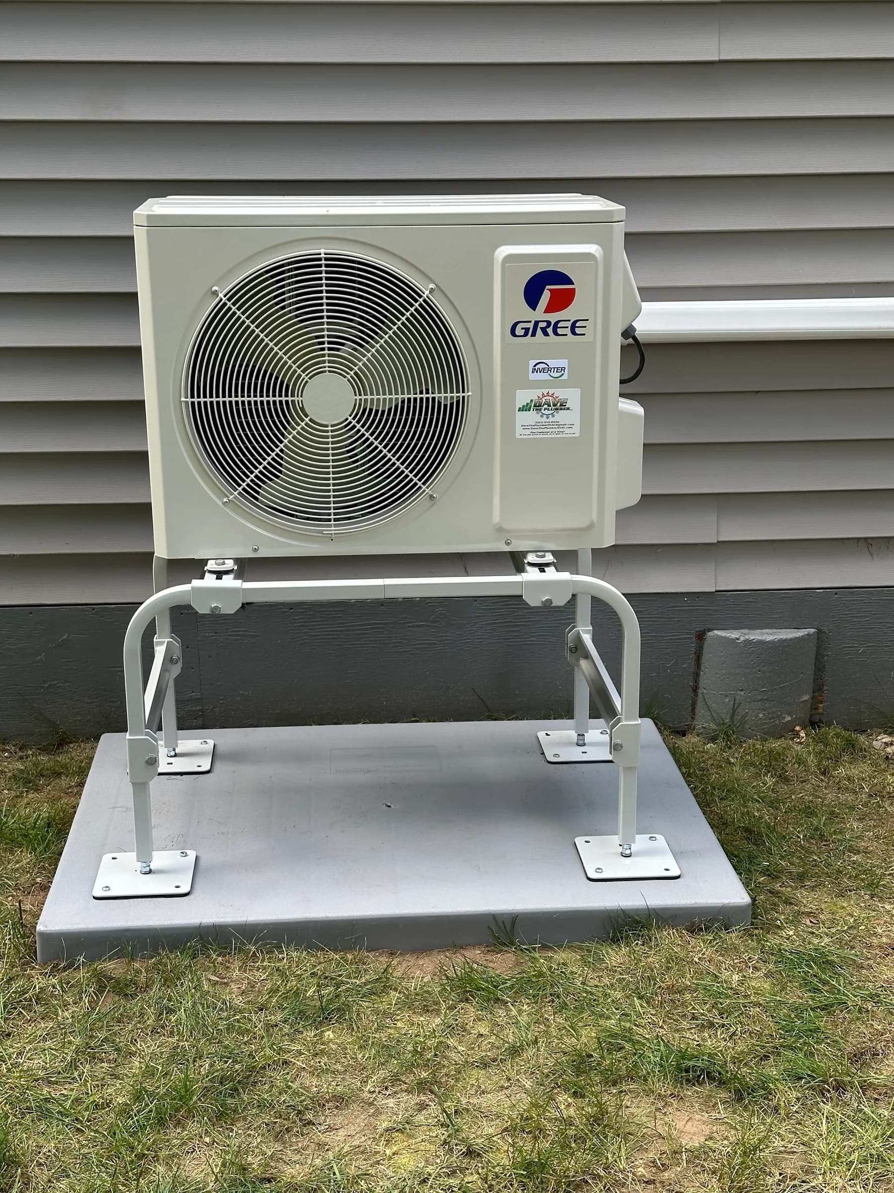 An outdoor heat pump unit on a galvanised wall stand above a concrete pad on a lawn