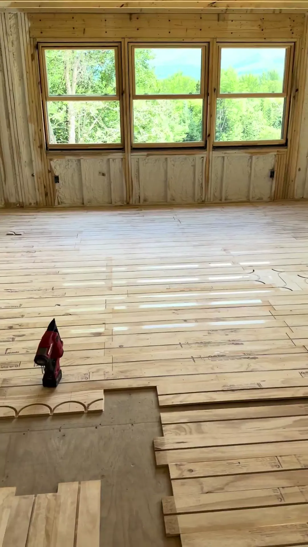 Radiant tubing laid across a full room of subfloor panels in front of a bank of three windows looking into trees