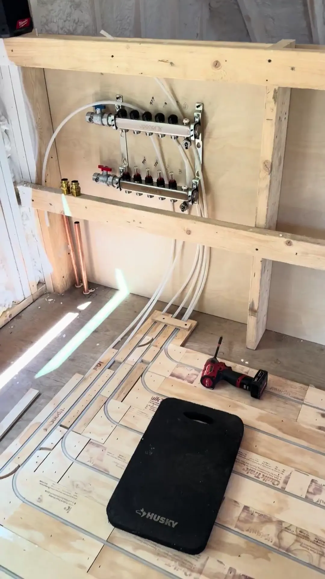 A radiant heating manifold on a stud wall with tubing loops running out across the subfloor below it