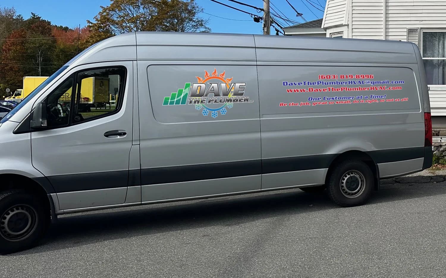 A branded service van parked on a residential street with autumn foliage behind it