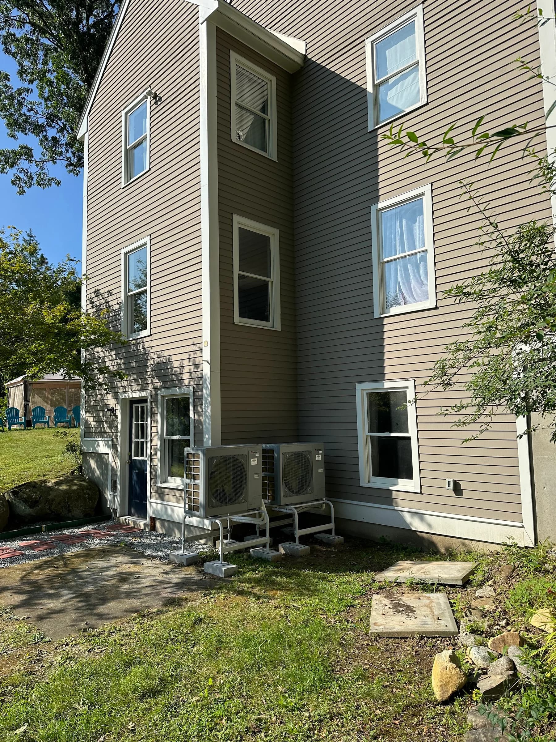 Two outdoor heat pump units at the base of a three story clapboard house