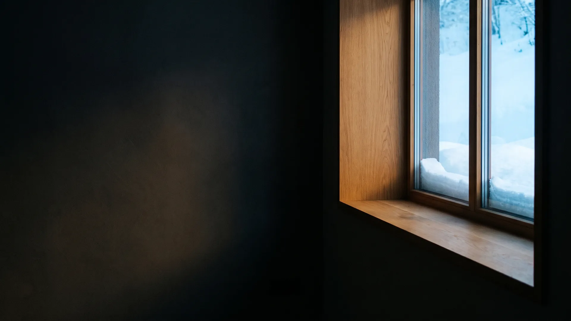 Snow banked on an exterior windowsill seen from inside a dim room
