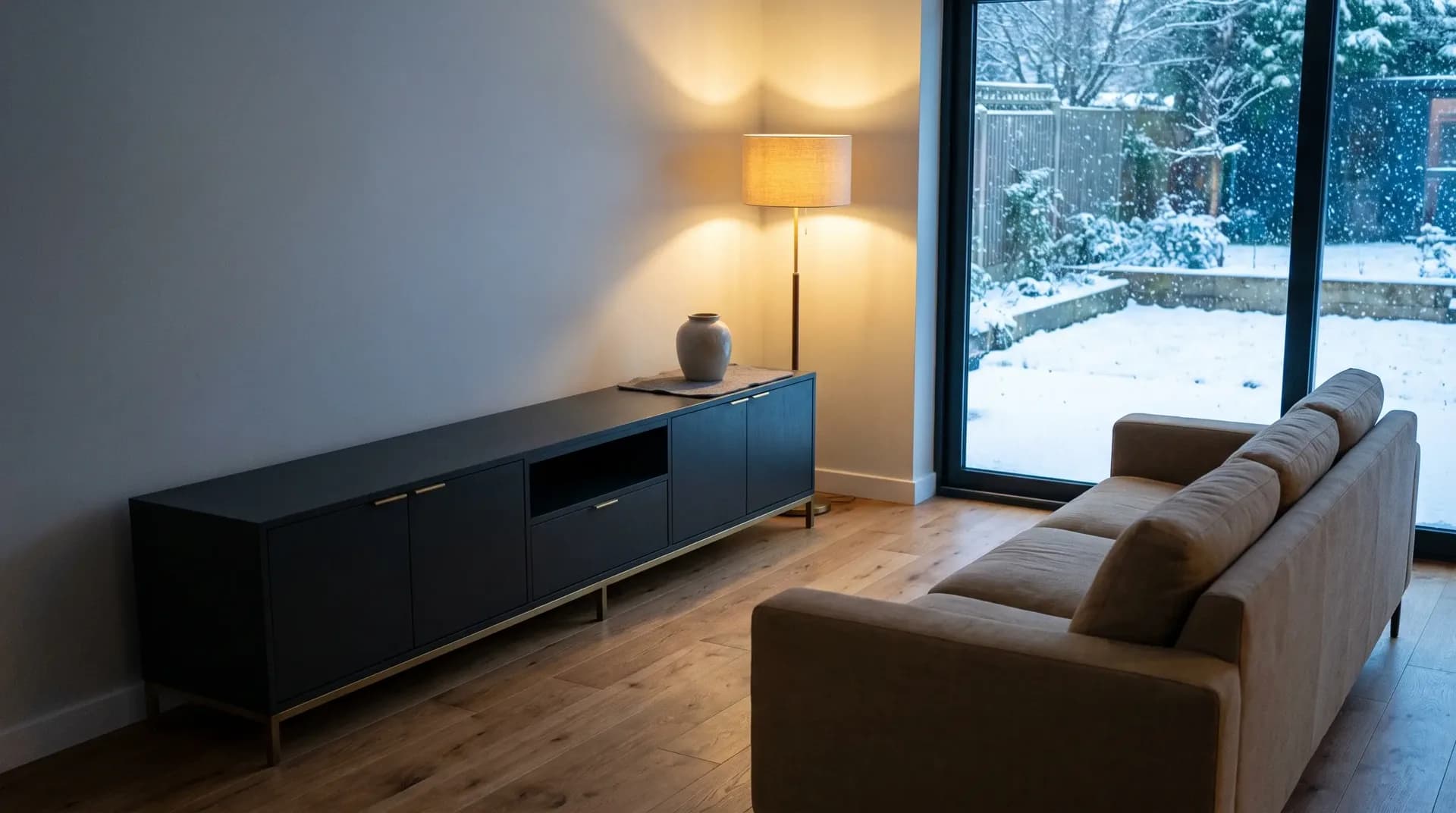 Living room with a green sofa and brass floor lamp beside a window with snow outside